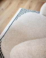 Lillian accent chair in natural fabric, shown from above at an angle highlighting the curved armrest and textured upholstery against hardwood flooring.