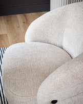 Lillian accent chair in natural fabric, showing curved rounded back and seat cushion from close-up side angle.