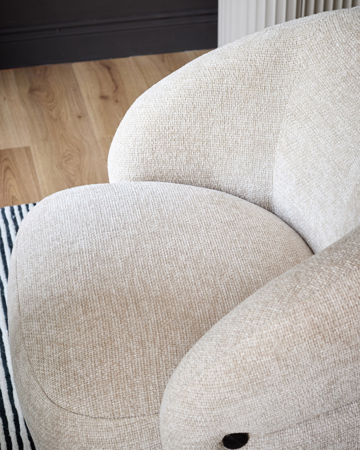 Lillian accent chair in natural fabric, showing curved rounded back and seat cushion from close-up side angle.