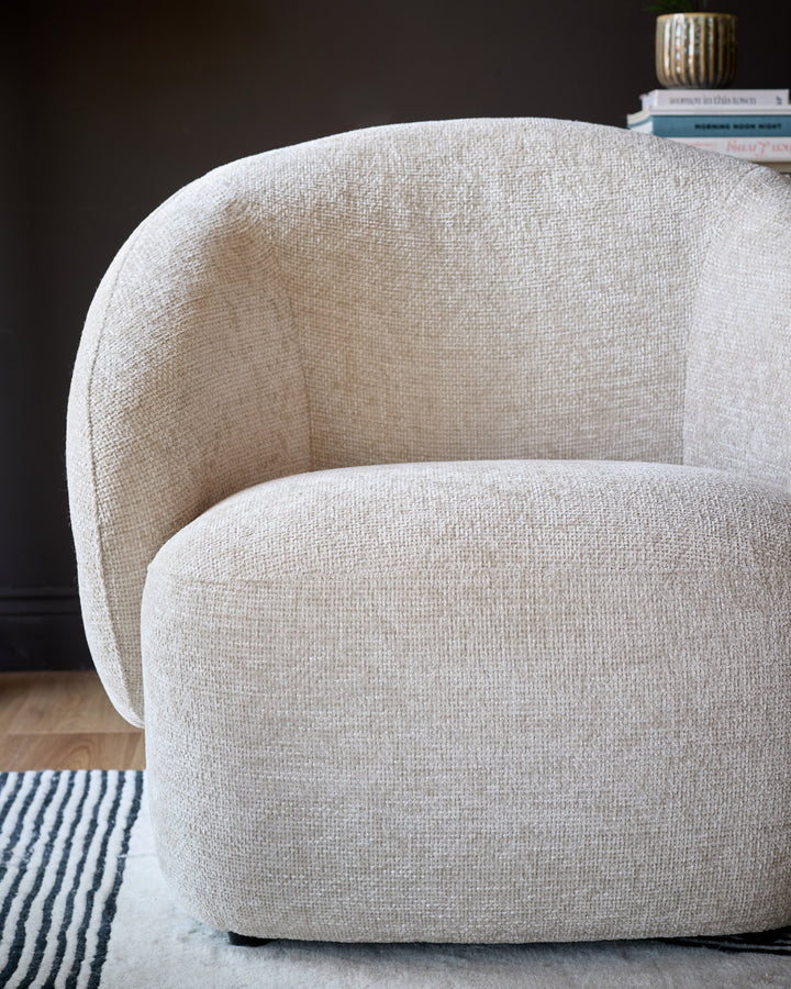 Lillian accent chair in natural fabric, rounded barrel shape with curved arms, side view on striped rug.