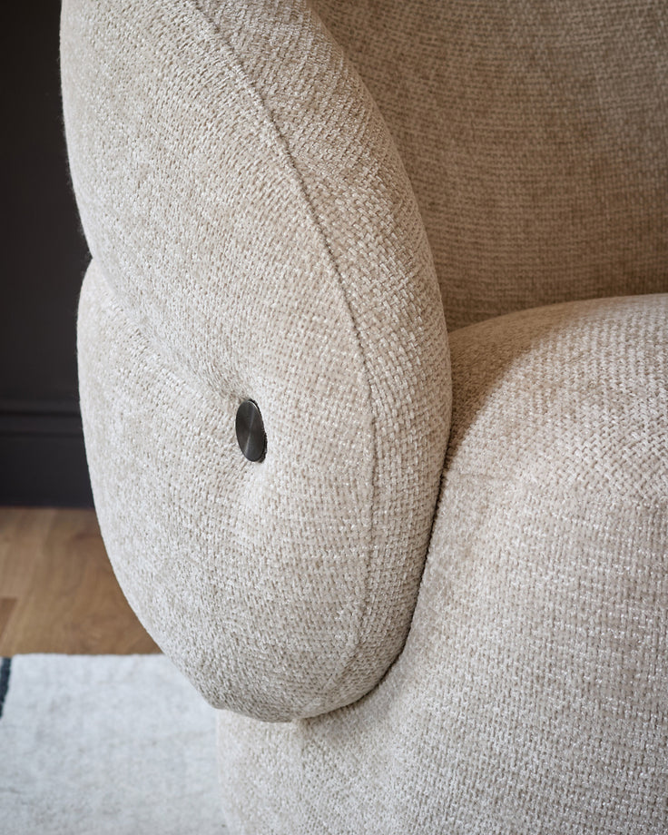Lillian accent chair in natural fabric, close-up of curved armrest with metal button detail.