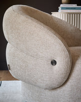 Lillian accent chair in natural fabric, showing curved backrest and rounded armrest with black metal handle detail.