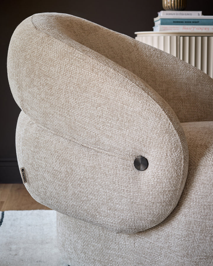 Lillian accent chair in natural fabric, showing curved backrest and rounded armrest with black metal handle detail.