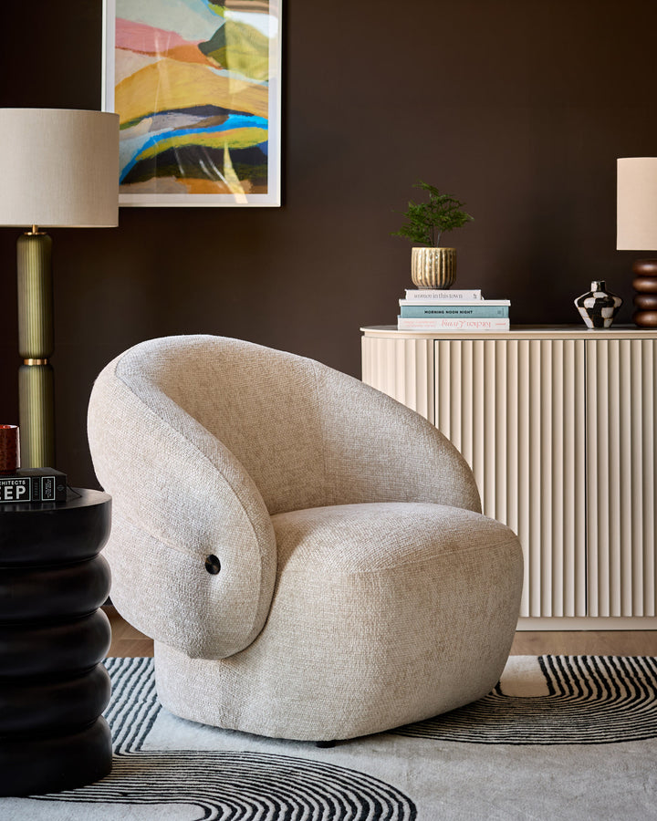 Lillian accent chair in natural fabric with curved, rounded silhouette and black button detail, displayed in modern room setting.