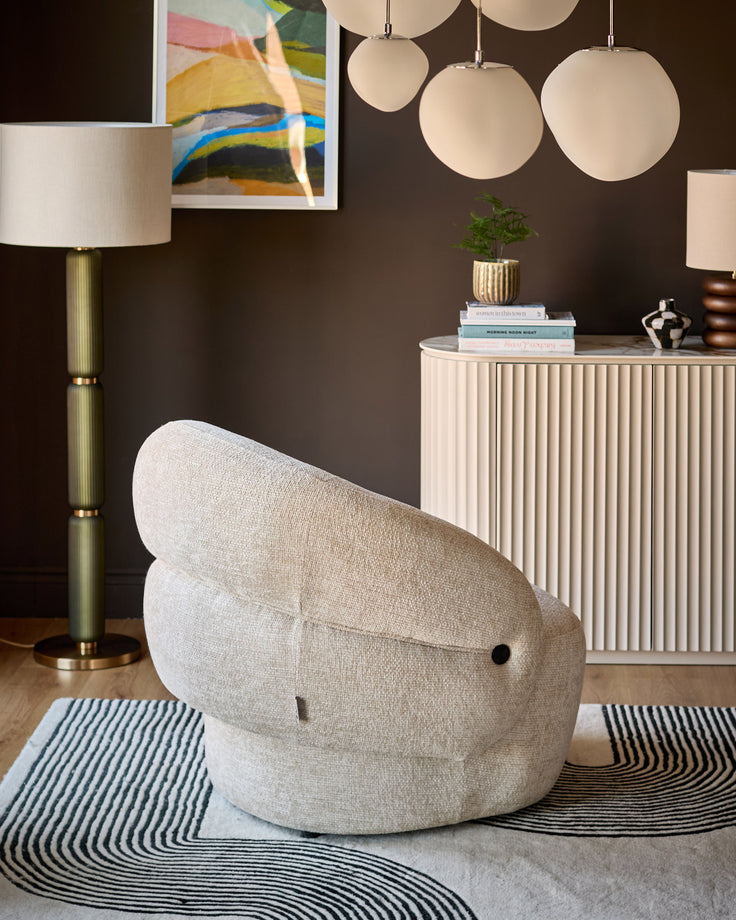 Lillian accent chair in natural fabric, shown in a styled living room setting with modern decor and dark walls.