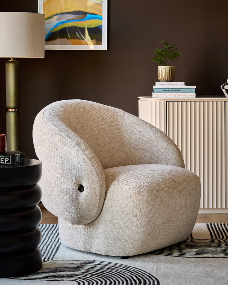 Lillian accent chair in natural fabric with curved, rounded shape and black button detail, shown in modern living room setting.