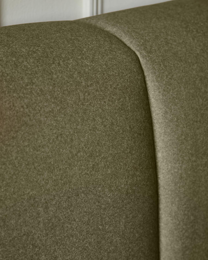 Olive green fabric ottoman bed showing curved headboard detail and soft upholstery texture from side angle.