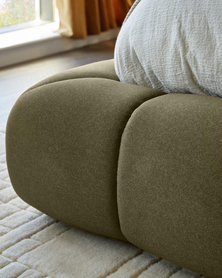 Olive green upholstered ottoman bed with rounded, curved design, shown in bedroom setting near window.