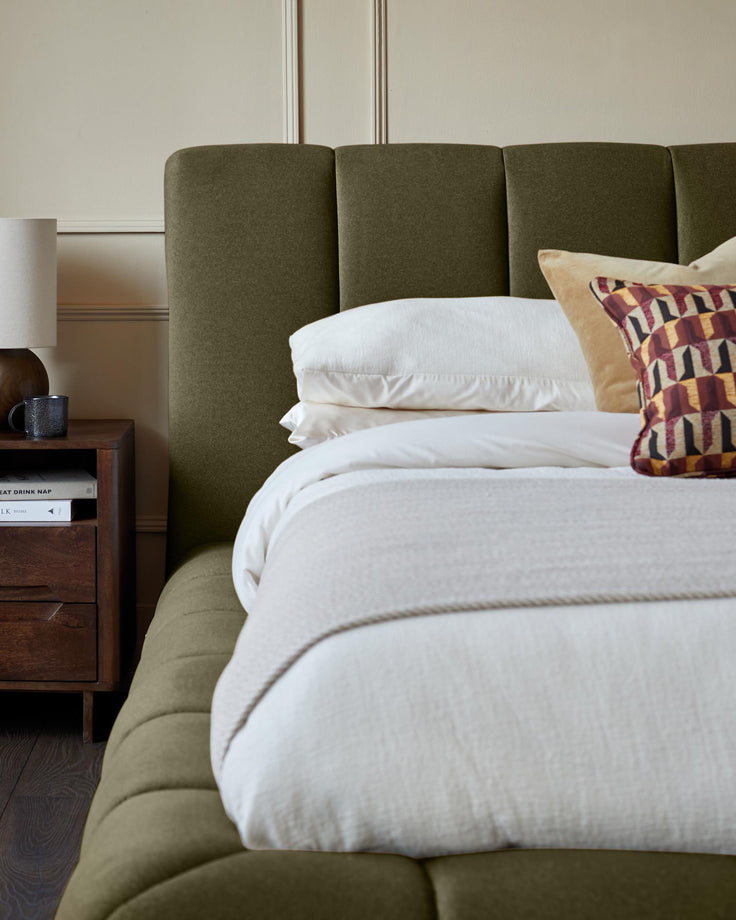 Lillian super king ottoman bed in olive green fabric, shown with white bedding and patterned cushions in bedroom setting.