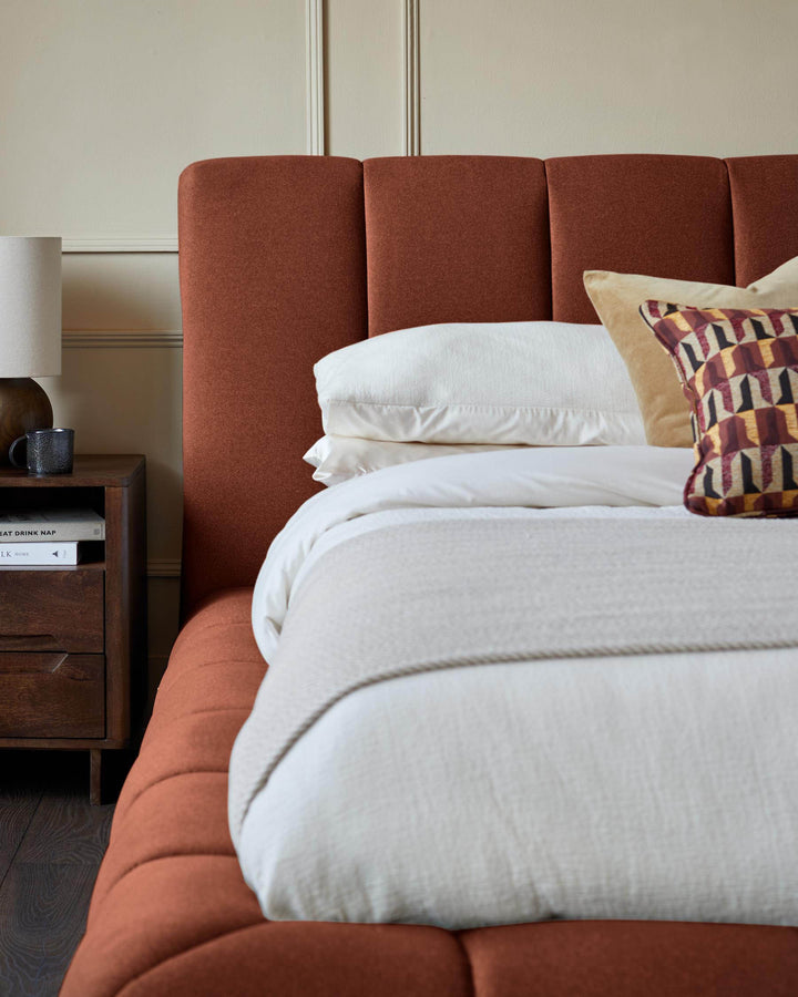 Lillian super king ottoman bed in toffee-red fabric with padded headboard, styled with white bedding and decorative pillows.