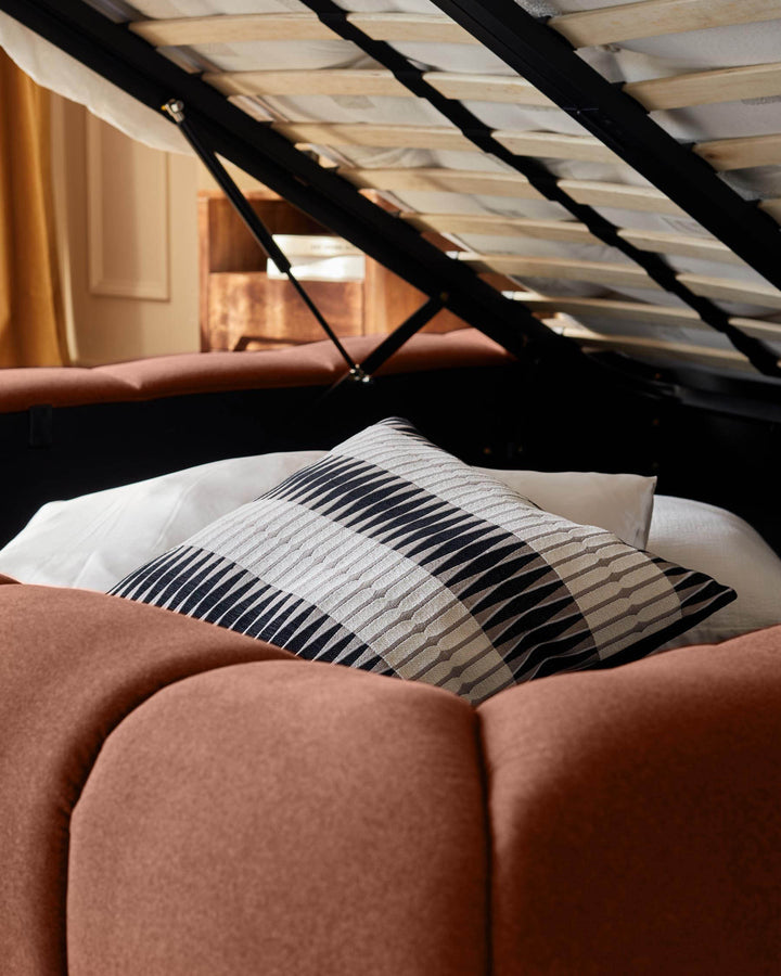 Toffee-red ottoman bed with striped pillow, angled attic room view with skylight.