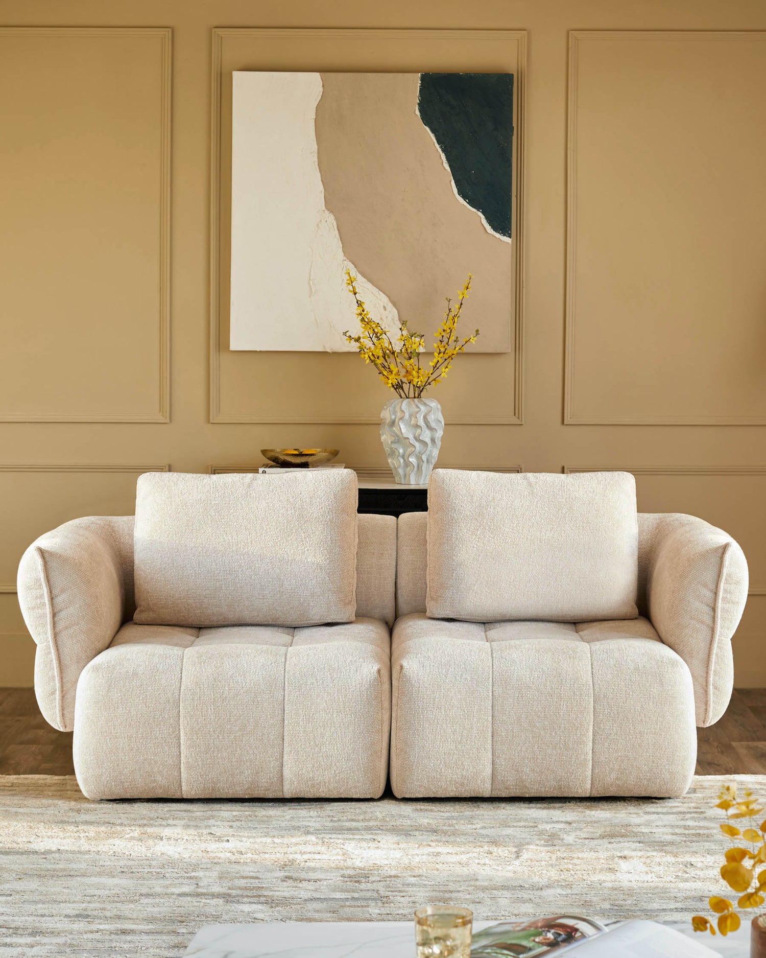 A neutral-toned modular sofa with cushions, complemented by a vase of yellow flowers and abstract art above.