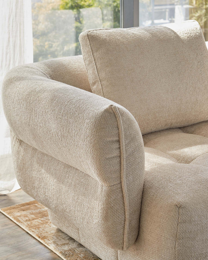 Textured beige sofa with plush cushions, featuring rounded arms and a modern design, set against a bright window view.