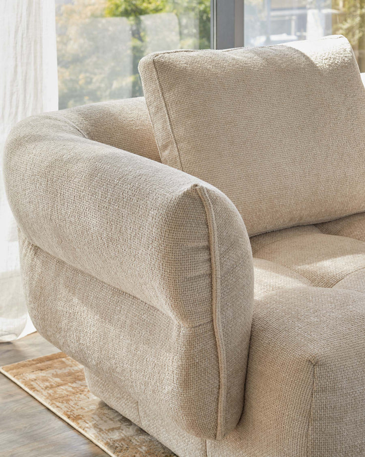 Textured beige sofa with plush cushions, featuring rounded arms and a modern design, set against a bright window view.