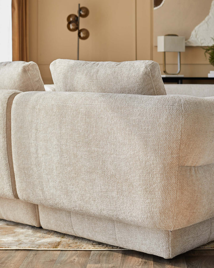 A plush, beige sectional sofa with soft cushions, featuring a textured fabric and clean lines, set against a stylish backdrop.