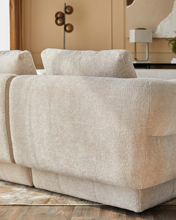A plush, beige sectional sofa with soft cushions, featuring a textured fabric and clean lines, set against a stylish backdrop.