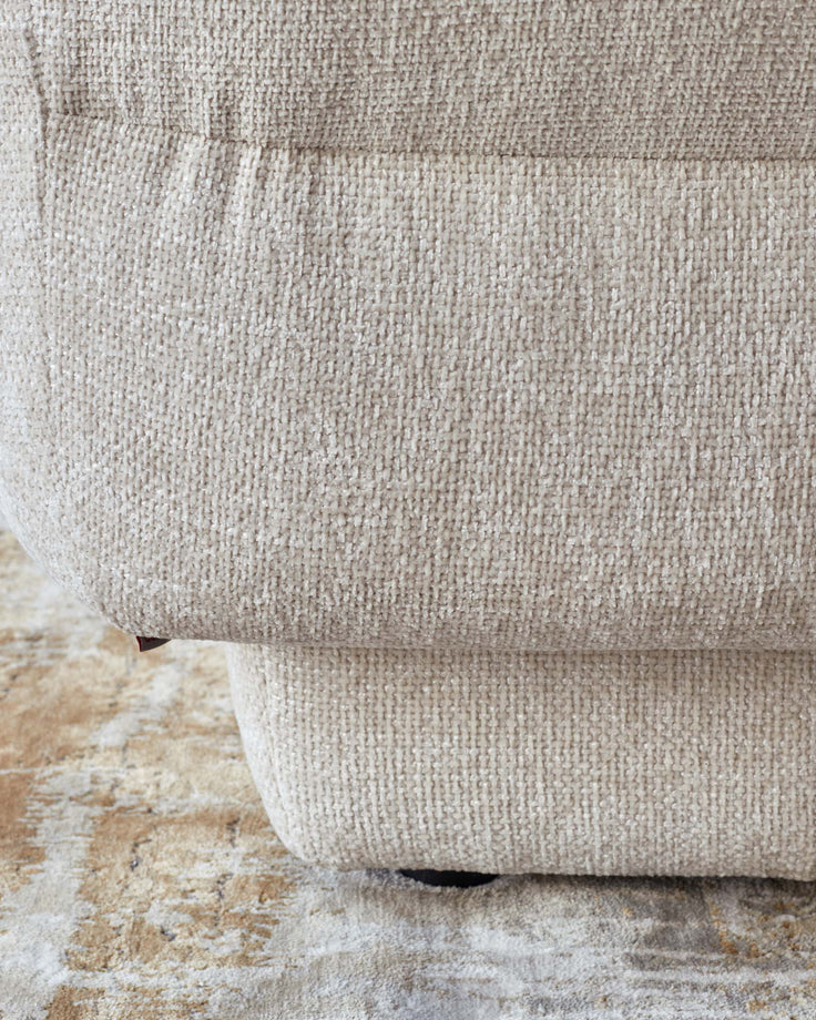 Textured beige sofa with a plush, comfortable design, resting on a patterned area rug in earthy tones.