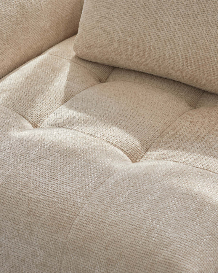 Beige, tufted upholstery fabric on a plush sofa with a soft texture, complemented by a matching cushion for added comfort.