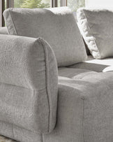 Lillian single-module sofa in light grey weave fabric, showing curved armrest and cushioned seat detail with windows in background.