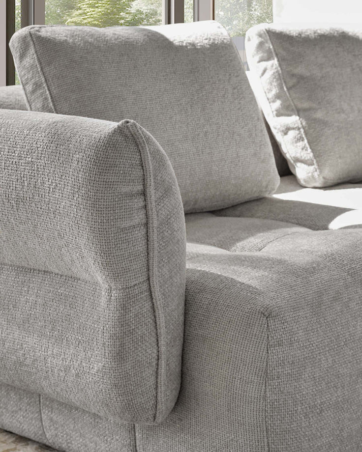 Lillian single-module sofa in light grey weave fabric, showing curved armrest and cushioned seat detail with windows in background.