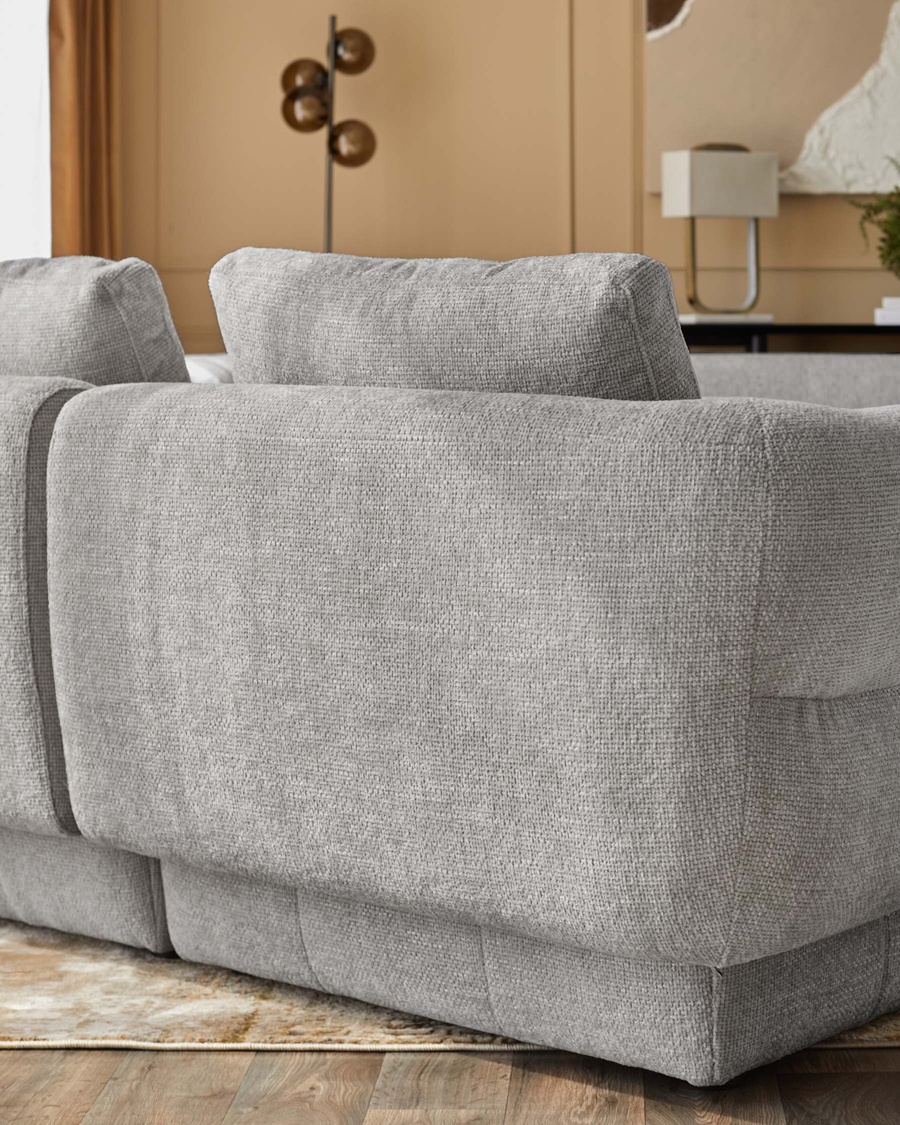 Lillian single-module sofa in light grey weave fabric, shown at side angle on wooden floor with beige wall backdrop.