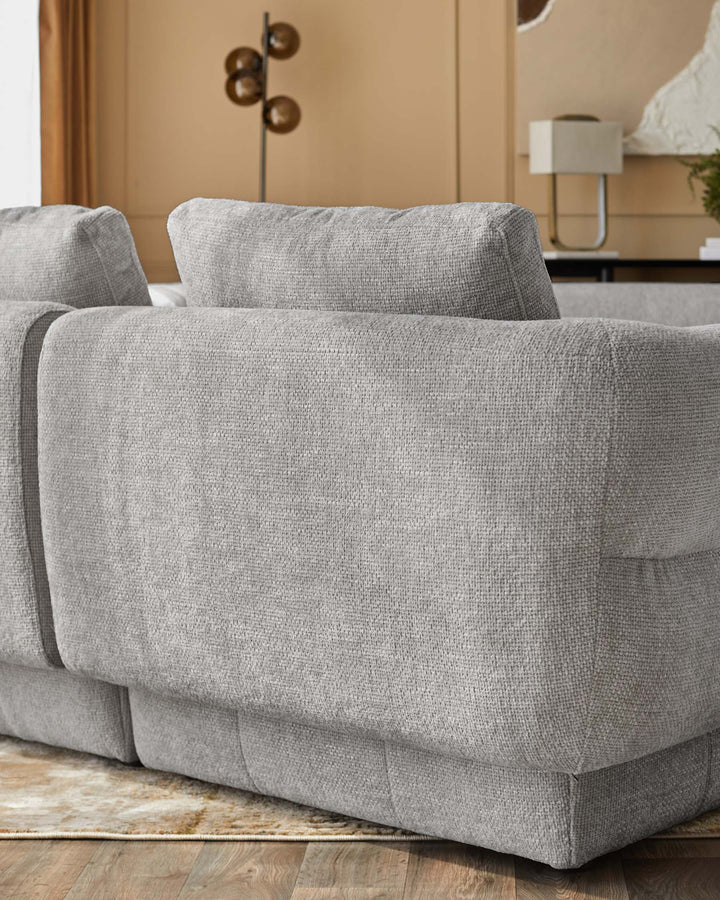 Lillian single-module sofa in light grey weave fabric, shown at side angle on wooden floor with beige wall backdrop.