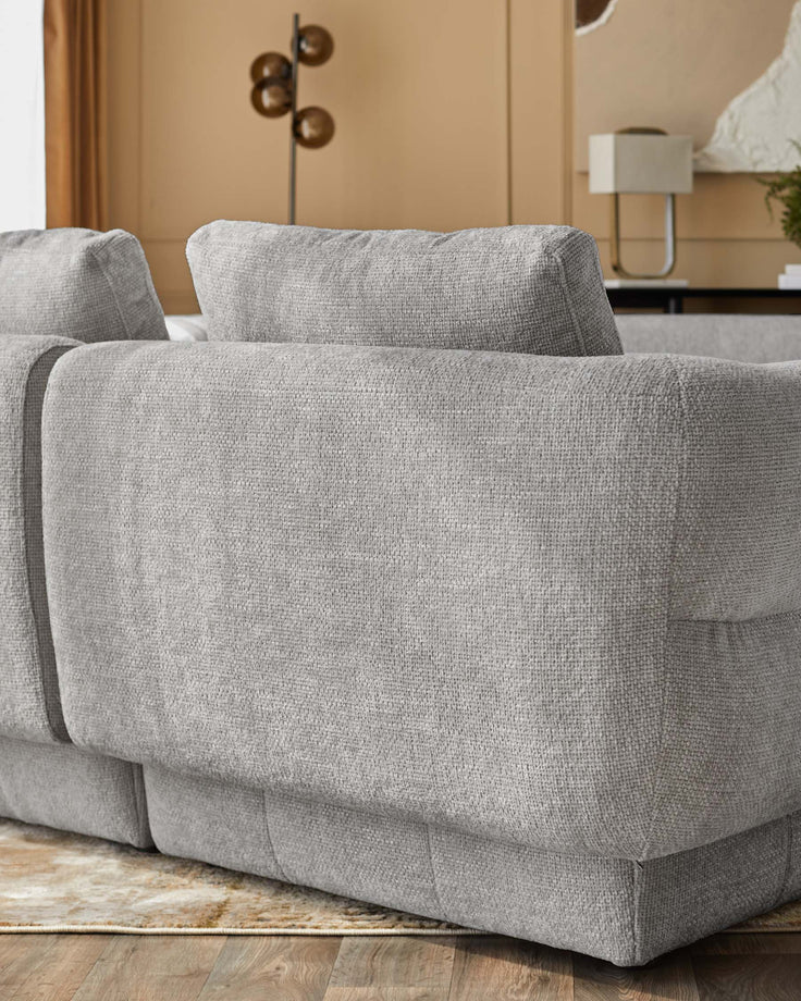 Lillian single-module sofa in light grey weave fabric, shown at side angle on wooden floor with beige wall backdrop.