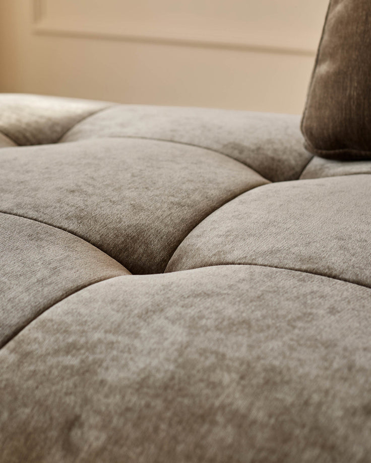 Close-up of a luxurious, beige, button-backed sofa, with a pillow resting on top, creating a comfortable and inviting seating area.