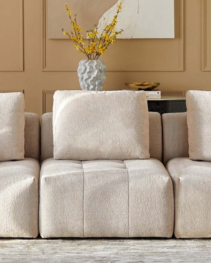 A beige modular sofa with a vase of yellow flowers displayed on top of it. Comfortable and stylish living room furniture.