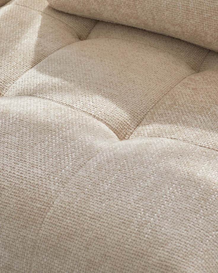 Close-up of a tufted, beige sofa. The fabric is textured and tightly woven.