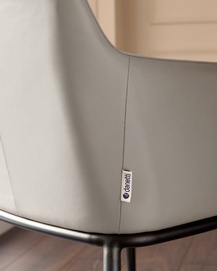 Logan dining chair in light grey real leather, close-up of seam and brand label on backrest.