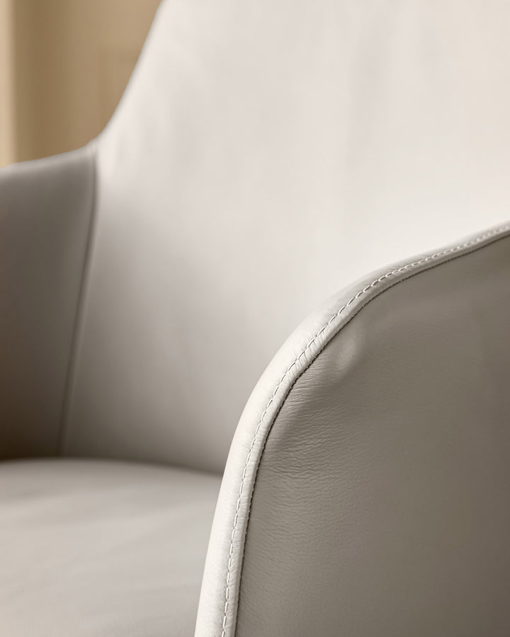 Logan dining chair in light grey leather, close-up of curved backrest and stitched seam detail.