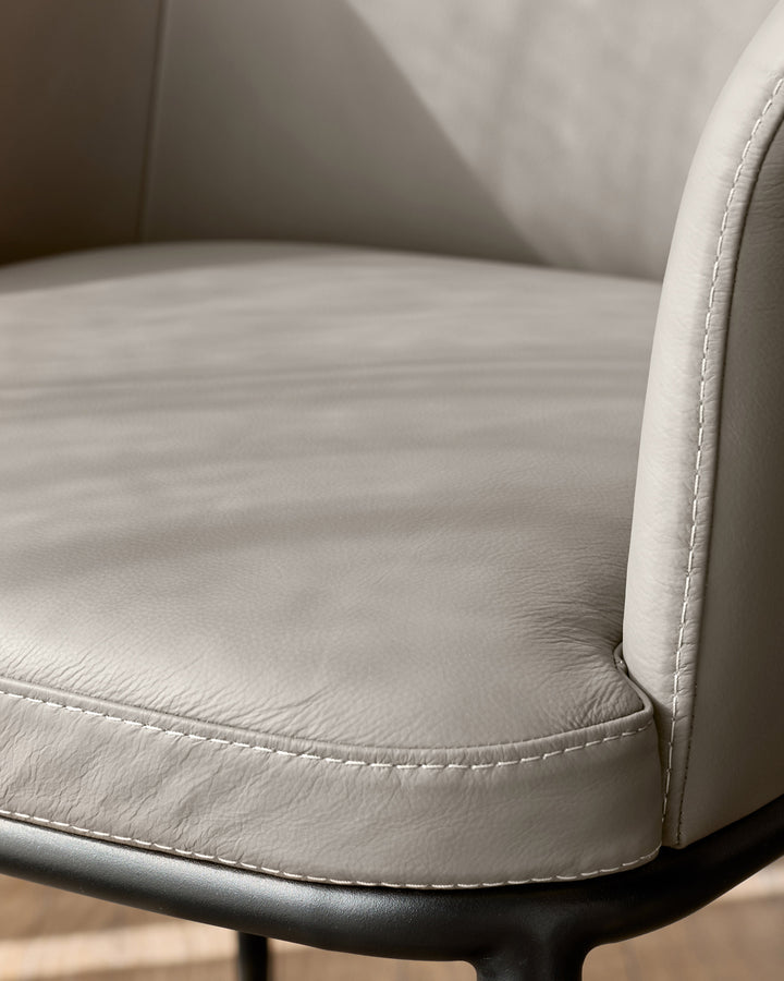 Logan dining chair in light grey leather, close-up of seat and armrest with contrast stitching detail.