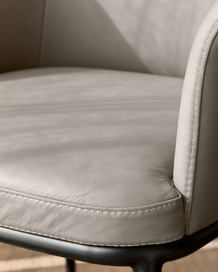 Logan dining chair in light grey leather, close-up of seat and armrest with contrast stitching detail.