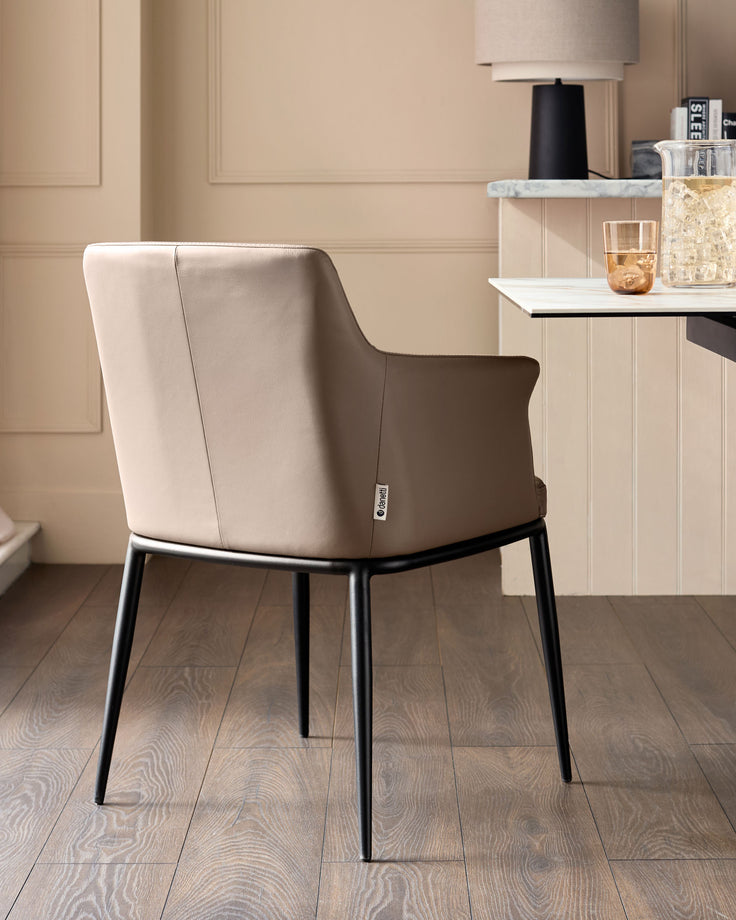Logan dining chair in mocha leather with black metal legs, shown from rear angle in a modern interior setting.
