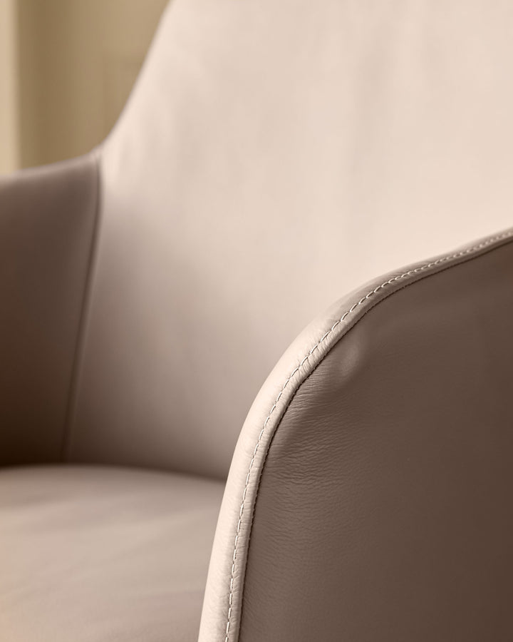 Logan dining chair in mocha leather, close-up detail showing stitched seam and curved backrest.