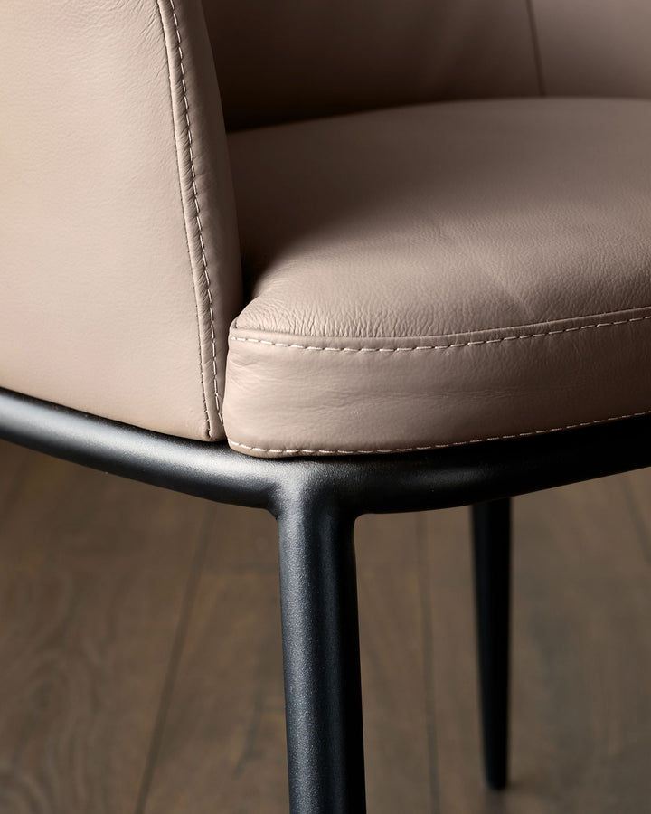 Logan dining chair in mocha leather with black metal legs, detail view showing stitched seat edge and armrest.