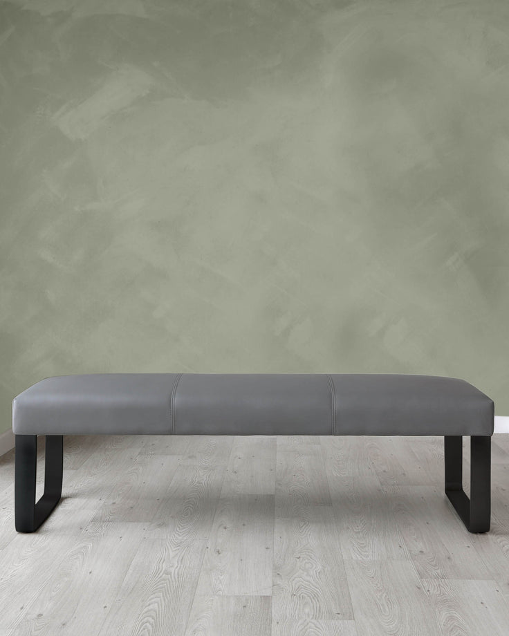 Modern minimalist grey upholstered bench with black legs, set on a light wooden floor against a textured green-grey wall.