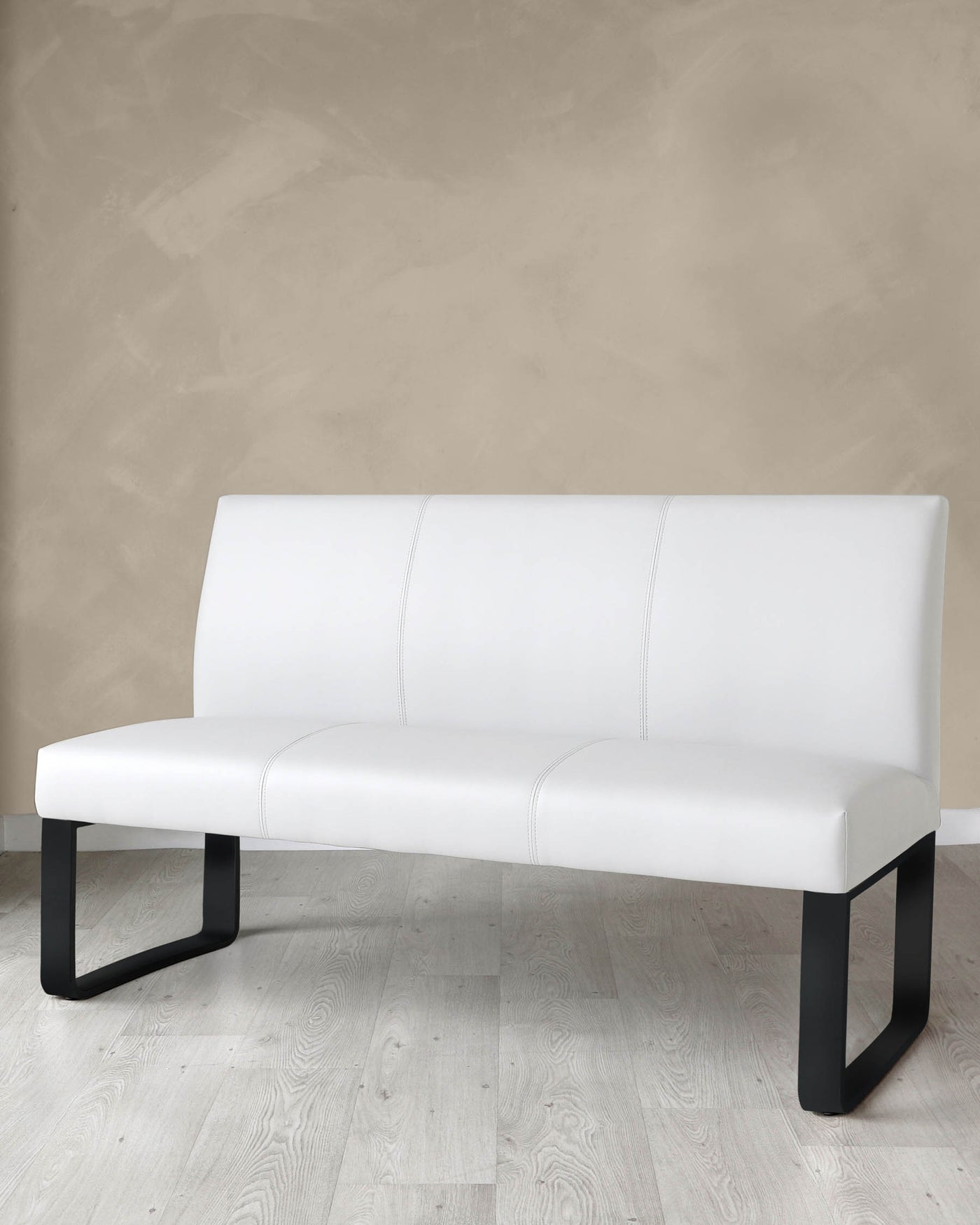 Modern white faux leather bench with a sleek minimalist design, featuring a single elongated cushion with subtle stitched detailing, and sturdy dark metal U-shaped legs, presented against a neutral-toned wall and on a light wooden floor.