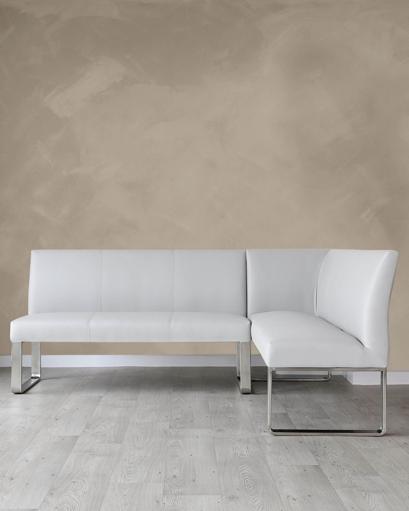 Modern L-shaped sectional sofa with white upholstery and sleek metal legs against a neutral wall on a light wooden floor.