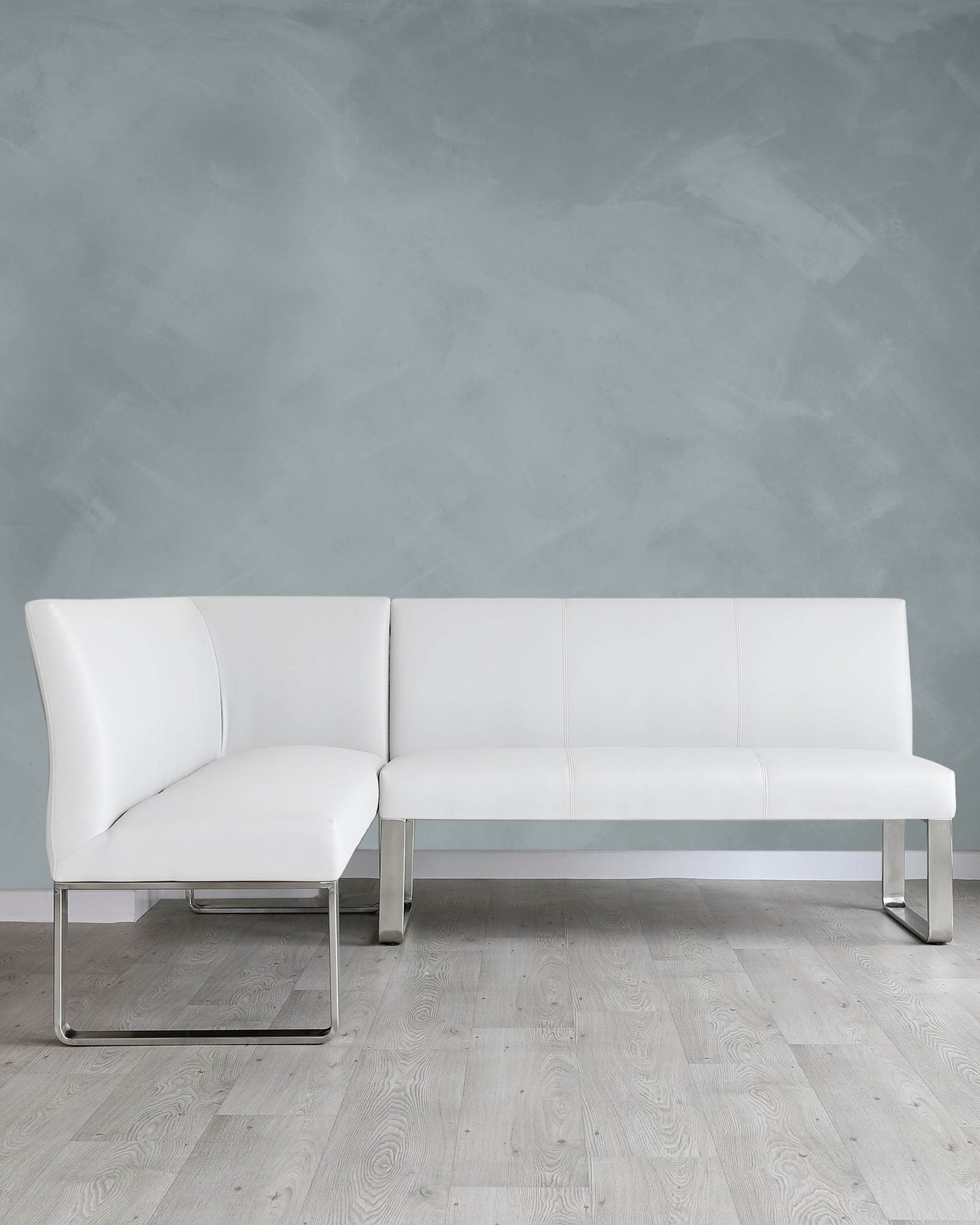 Modern white leather sectional sofa with chrome legs on a light wooden floor against a textured grey wall.