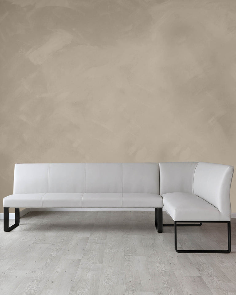 Modern L-shaped sectional sofa with white upholstery and a minimalist black metal frame, situated on a light wooden floor against a textured beige wall.