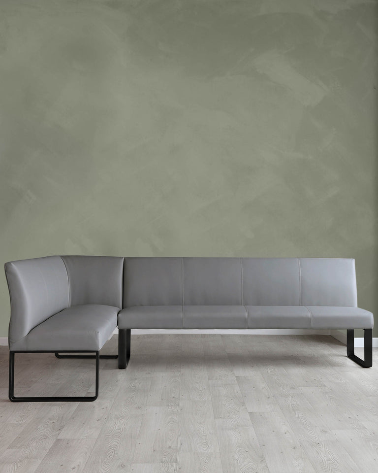 Modern minimalist L-shaped sectional sofa with a sleek silhouette, upholstered in light grey leather and supported by a black metal frame, against a textured sage green wall on a light wood herringbone floor.
