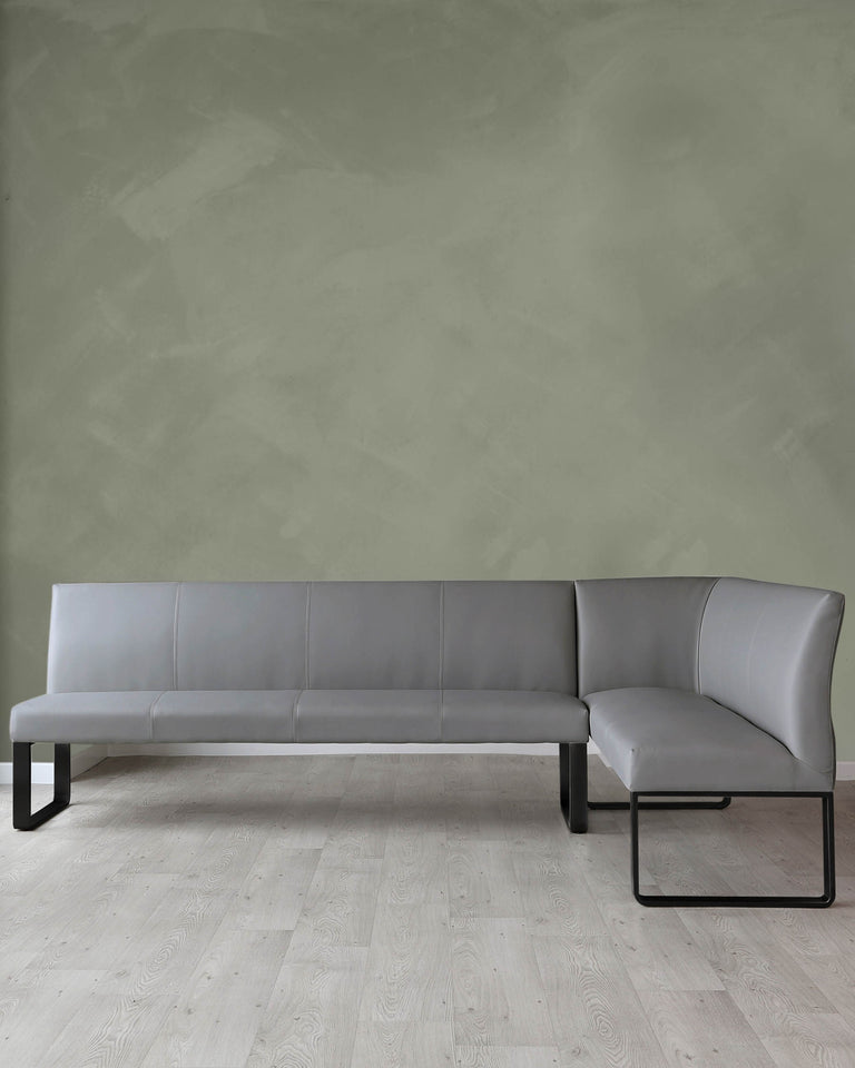Modern minimalist grey sectional sofa with sleek black metal legs, featuring a straight clean-lined design and a chaise lounge extension, set against a textured green wall and light hardwood flooring.