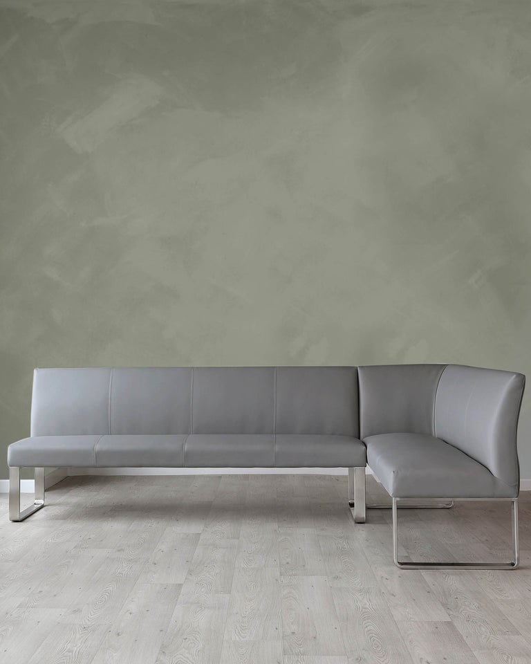 Modern L-shaped grey leather sectional sofa with a minimalist design, featuring clean lines, a low backrest, and sleek metallic legs, set on a light wooden floor against a textured olive-green wall.