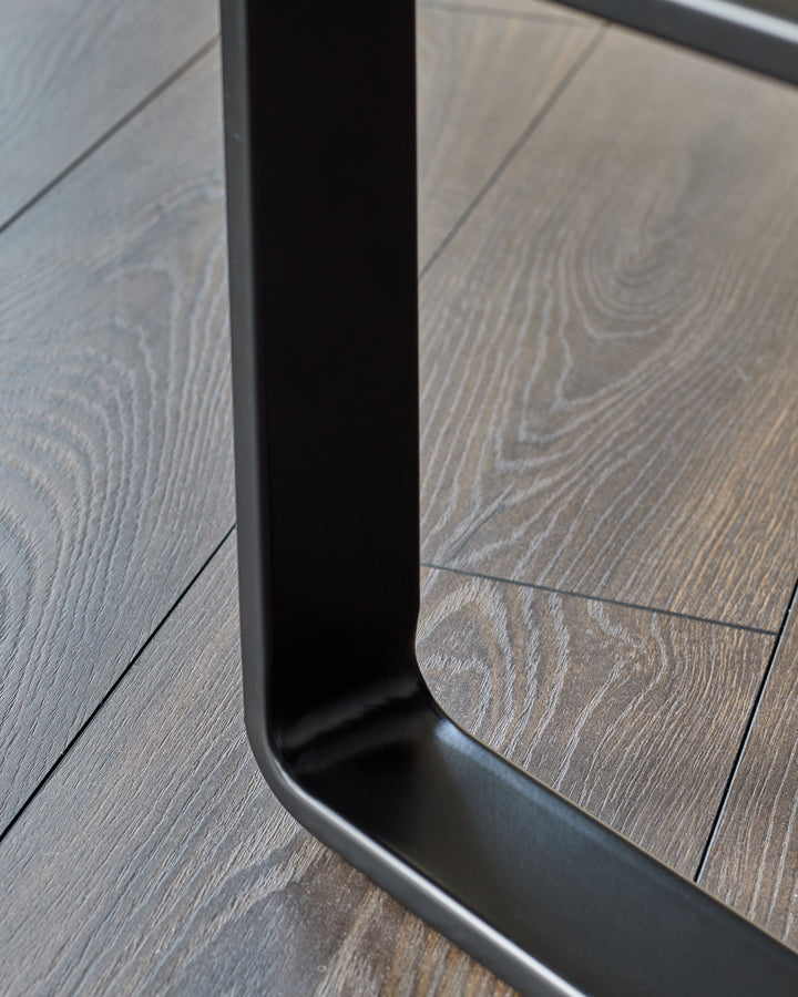 Black metal loop handle detail on olive-green velvet bench leg, close-up shot on wood floor.
