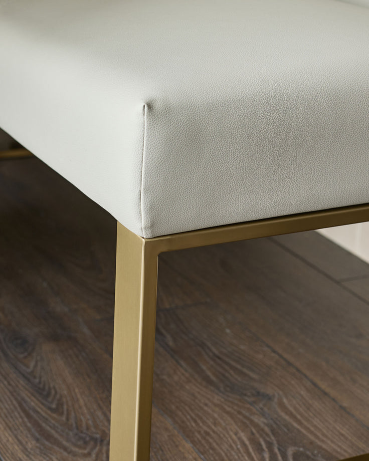 Light grey faux leather bench with brushed brass leg, close-up detail view.