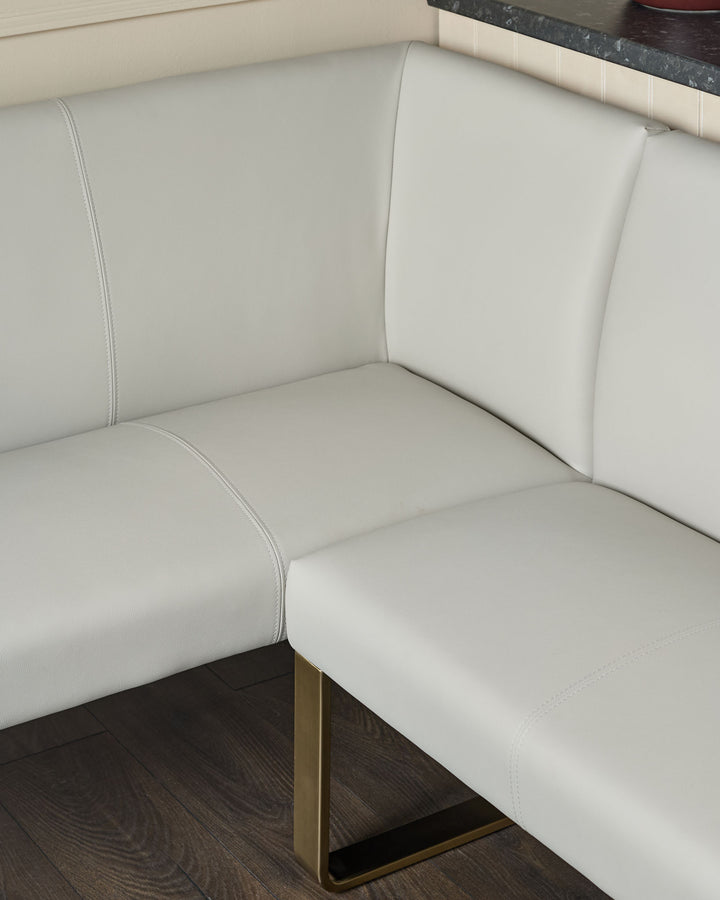 Light grey faux leather corner dining bench with brushed brass leg, showing seat and backrest detail.
