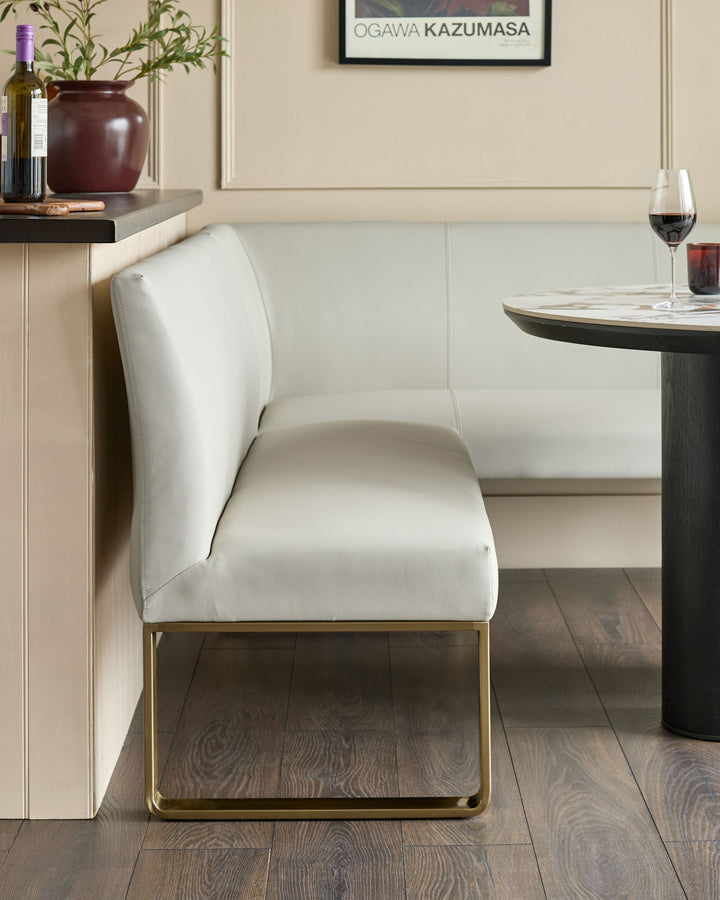 White faux leather dining chair with curved backrest and brushed brass legs, shown in modern dining room setting.
