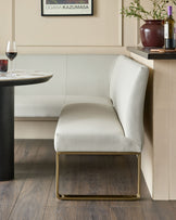 White faux leather dining chair with brushed brass legs, shown in a modern dining setting next to a round table.